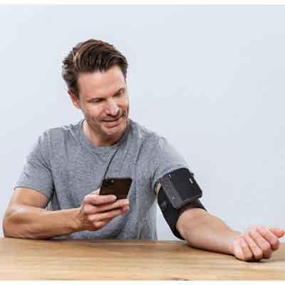 Image of a Beurer BM 81 user with monitor on the upper arm and holding smartphone with beurer HealthManager app 