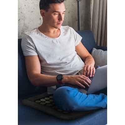 Image of user of UTK heat pad sitting on a couch and using a laptop